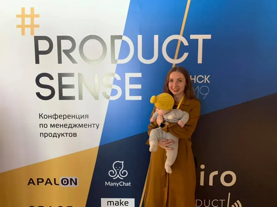 Nadia Nazarova holding her baby daughter in front of the Product Sense conference backdrop